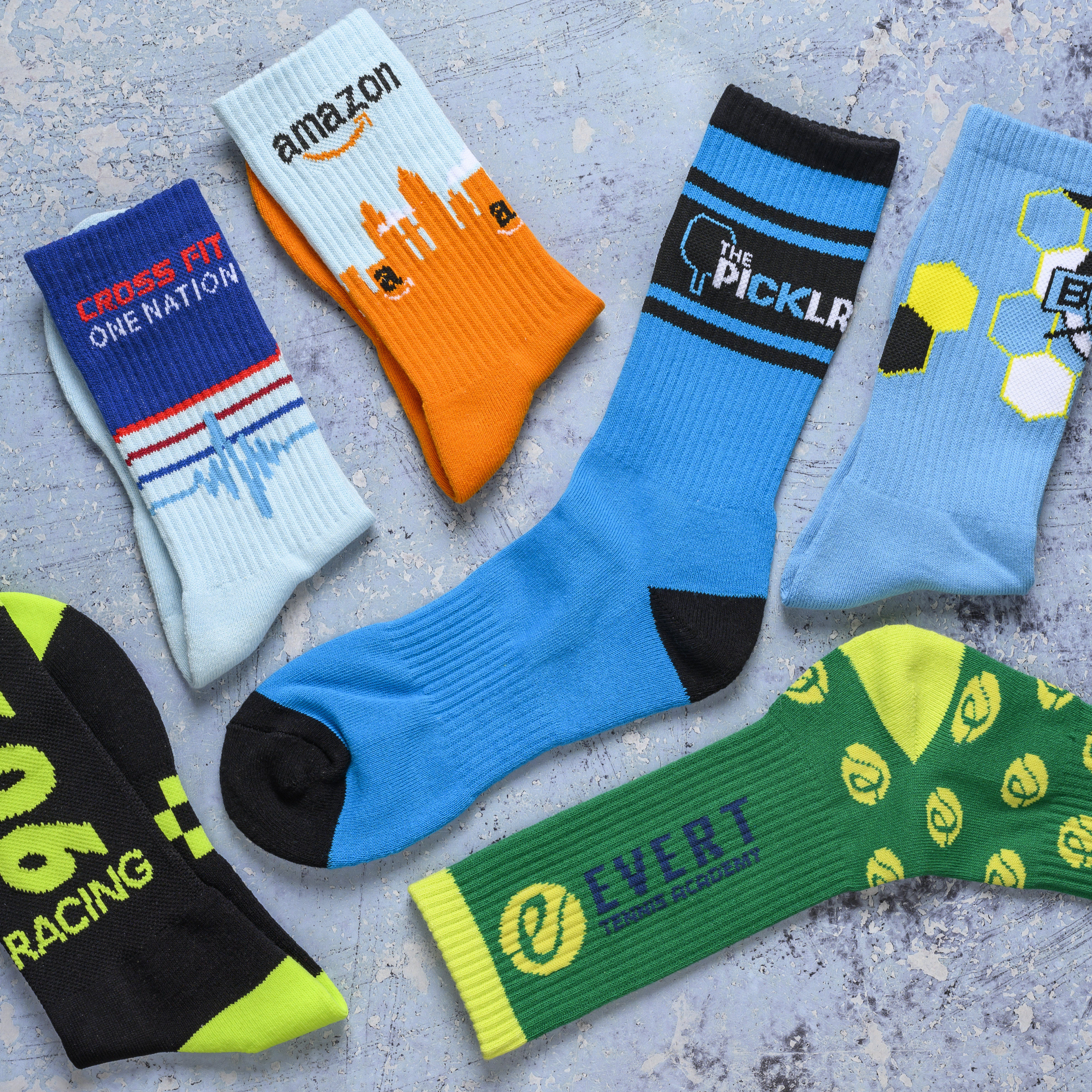 An overhead shot of multiple pairs of colorful, custom-branded crew socks on a gray surface.