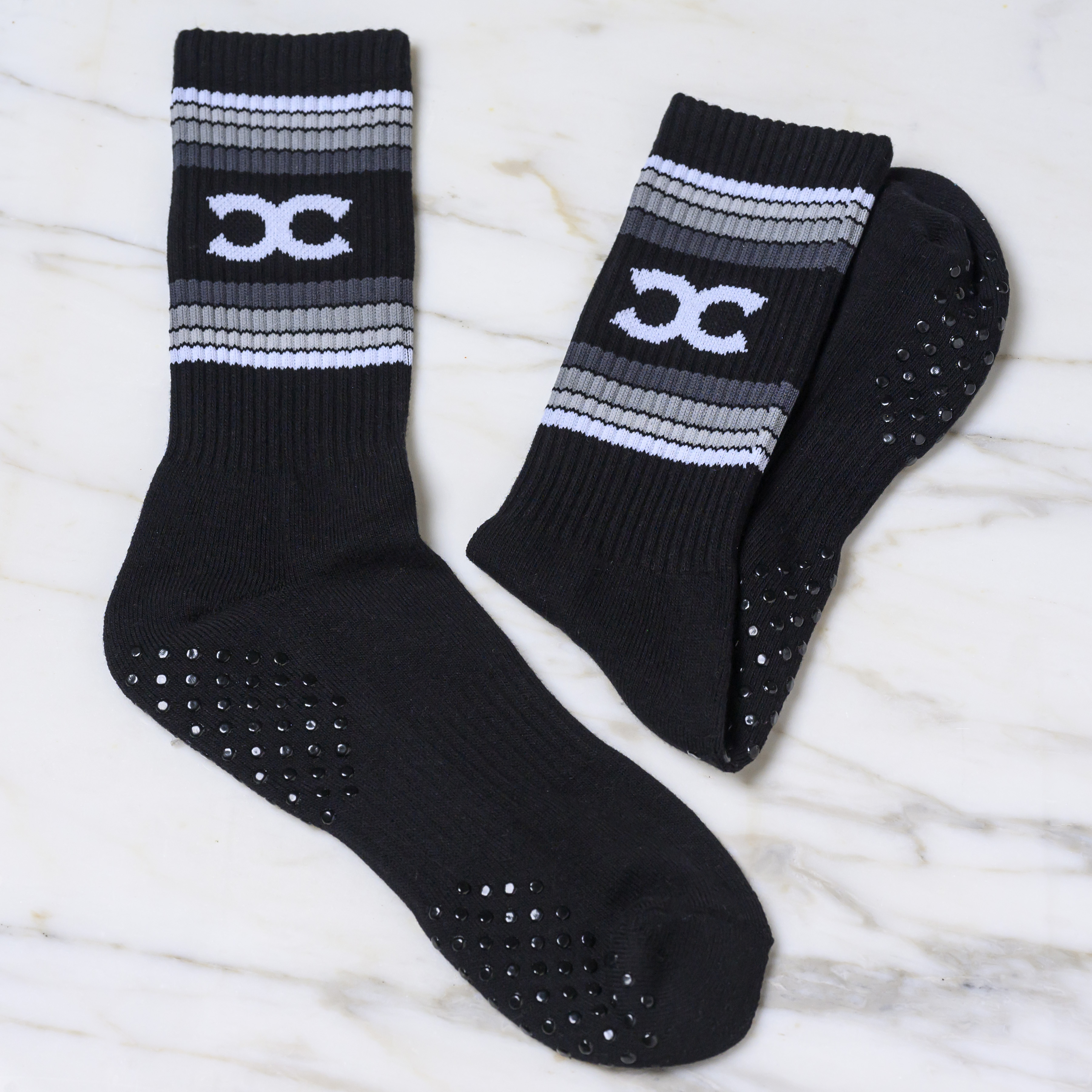 A pair of black athletic socks with grey and white stripes and non-slip grips on the soles.