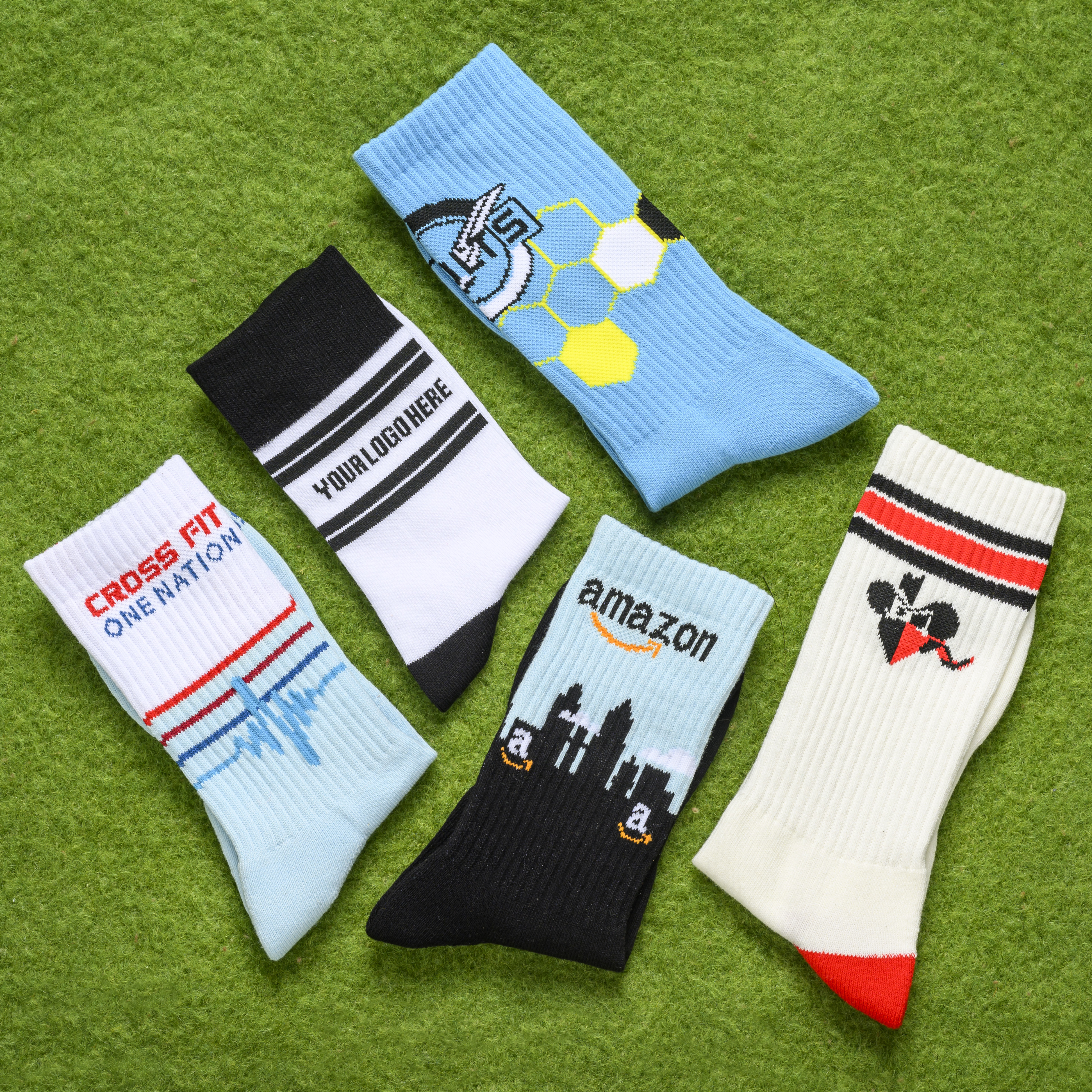 An overhead view of five different custom athletic socks laid out on a green, grassy surface.