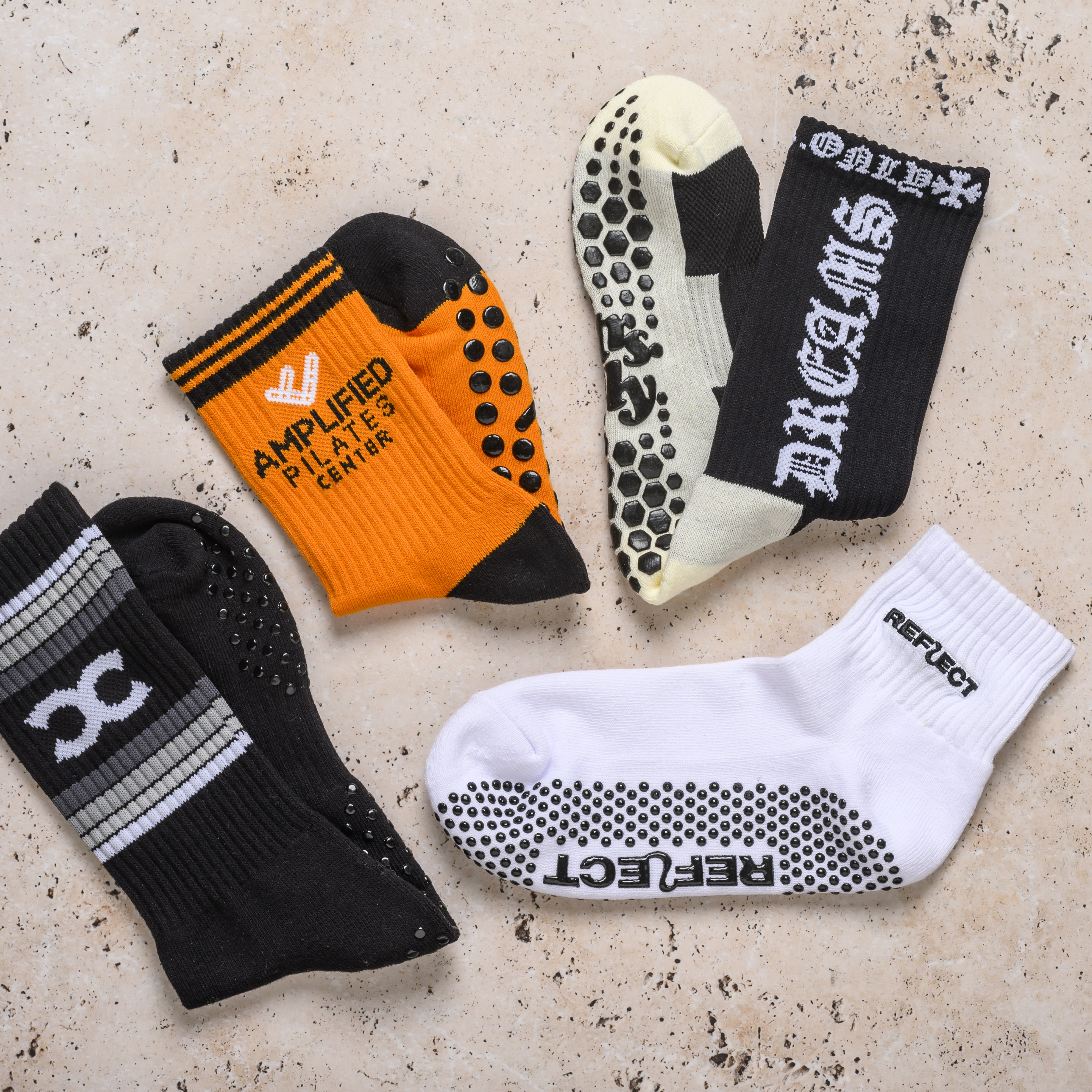 Four different pairs of branded athletic grip socks laid out on a stone surface.