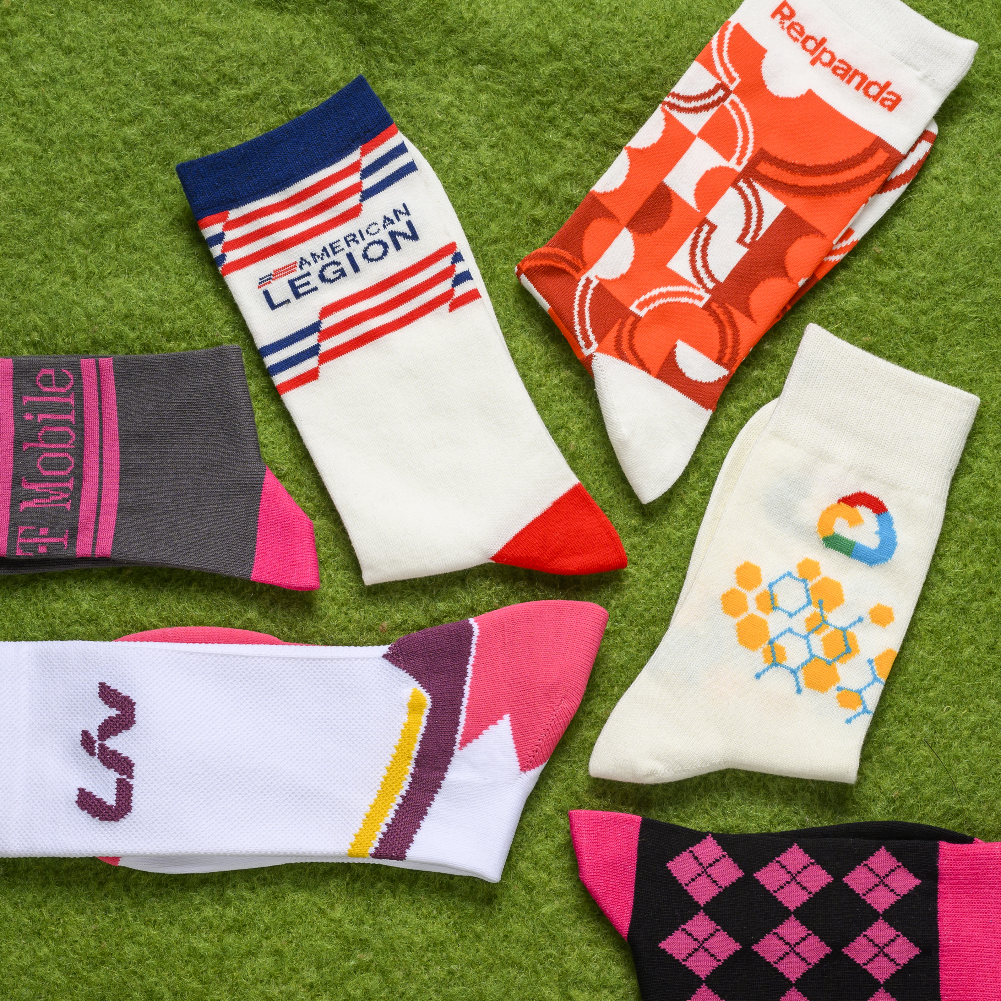 A collection of colorful custom branded socks displayed on a green textured surface.