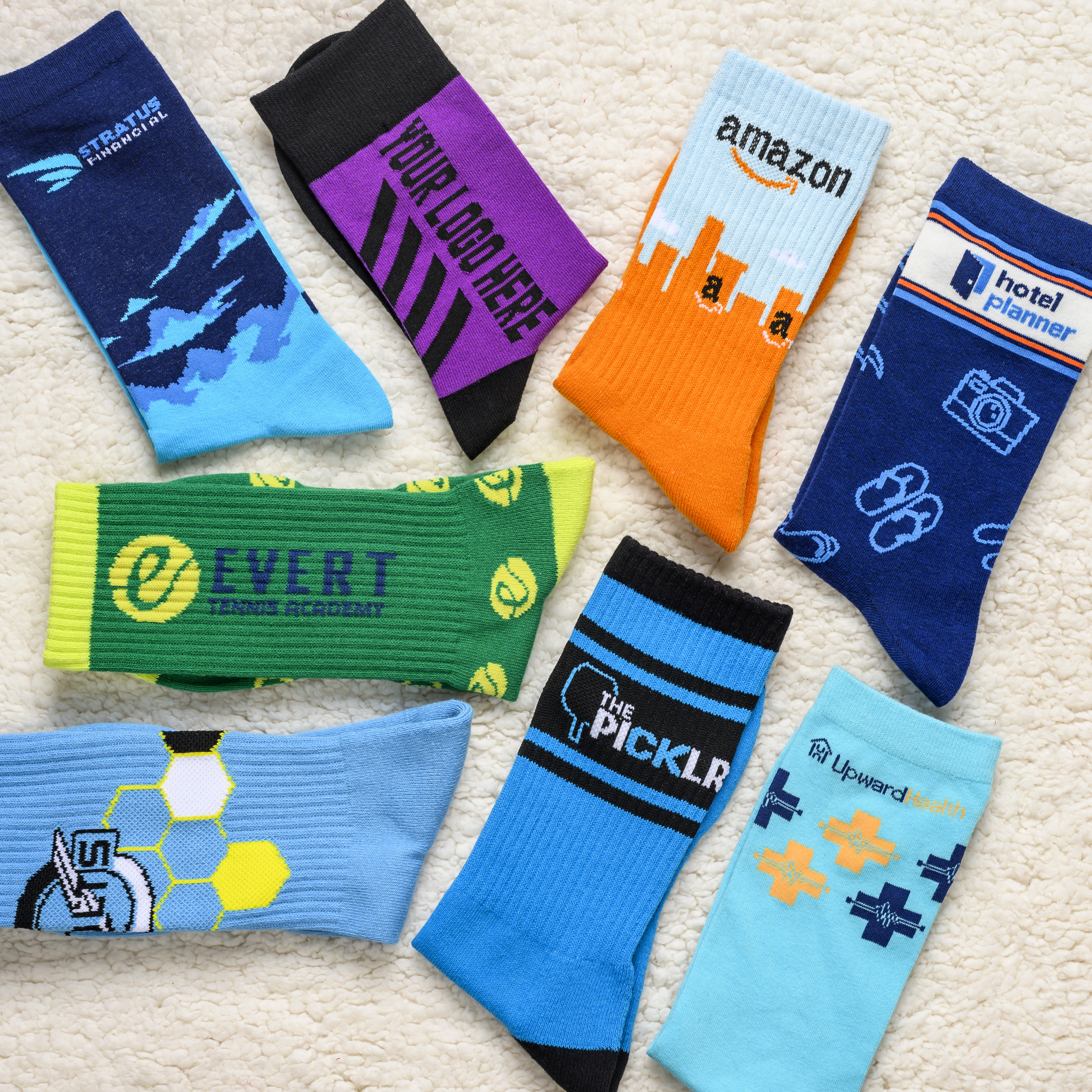 An assortment of colorful custom-branded socks with various logos laid out on a fluffy white surface.