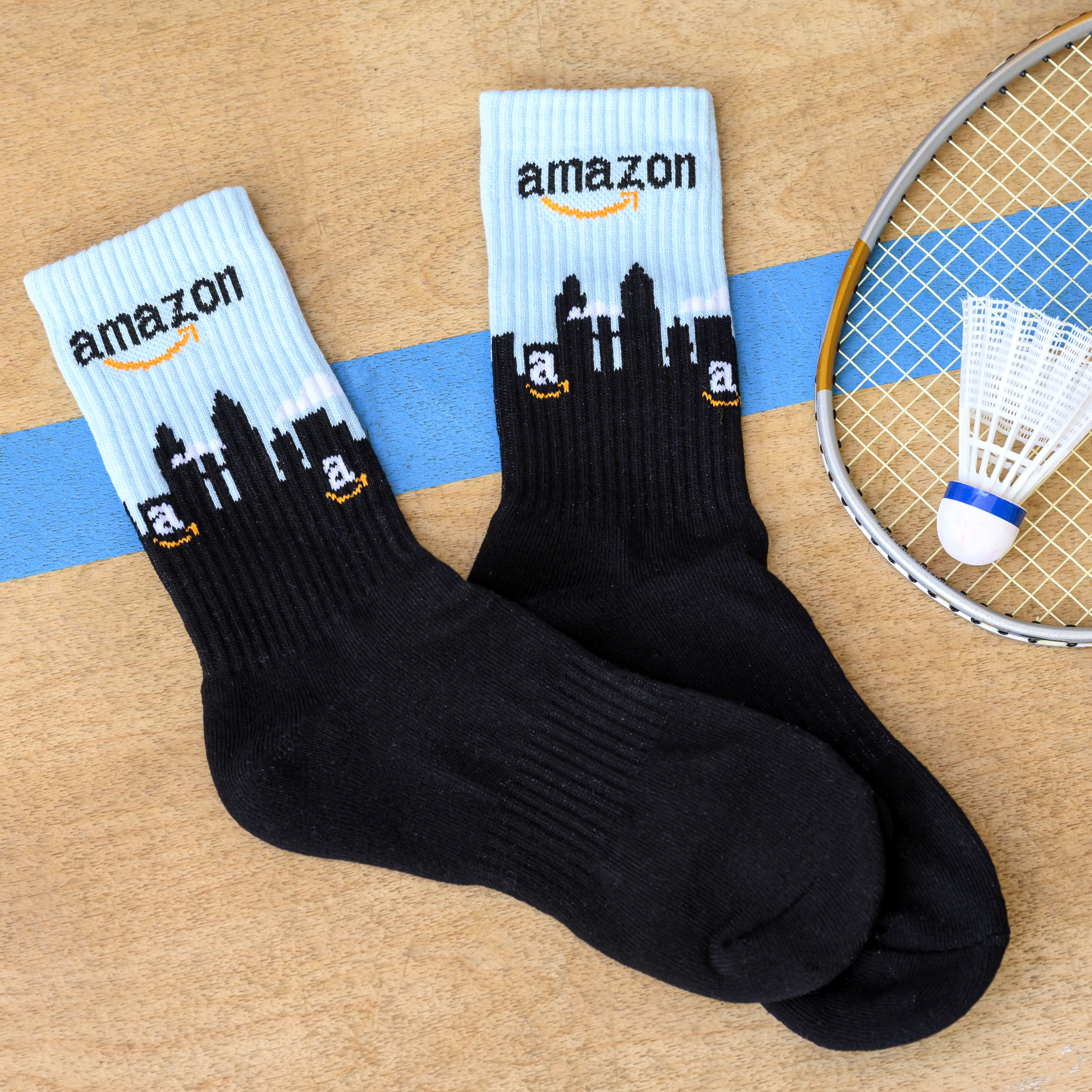 A pair of Amazon branded socks with a city skyline next to a badminton racket and shuttlecock.