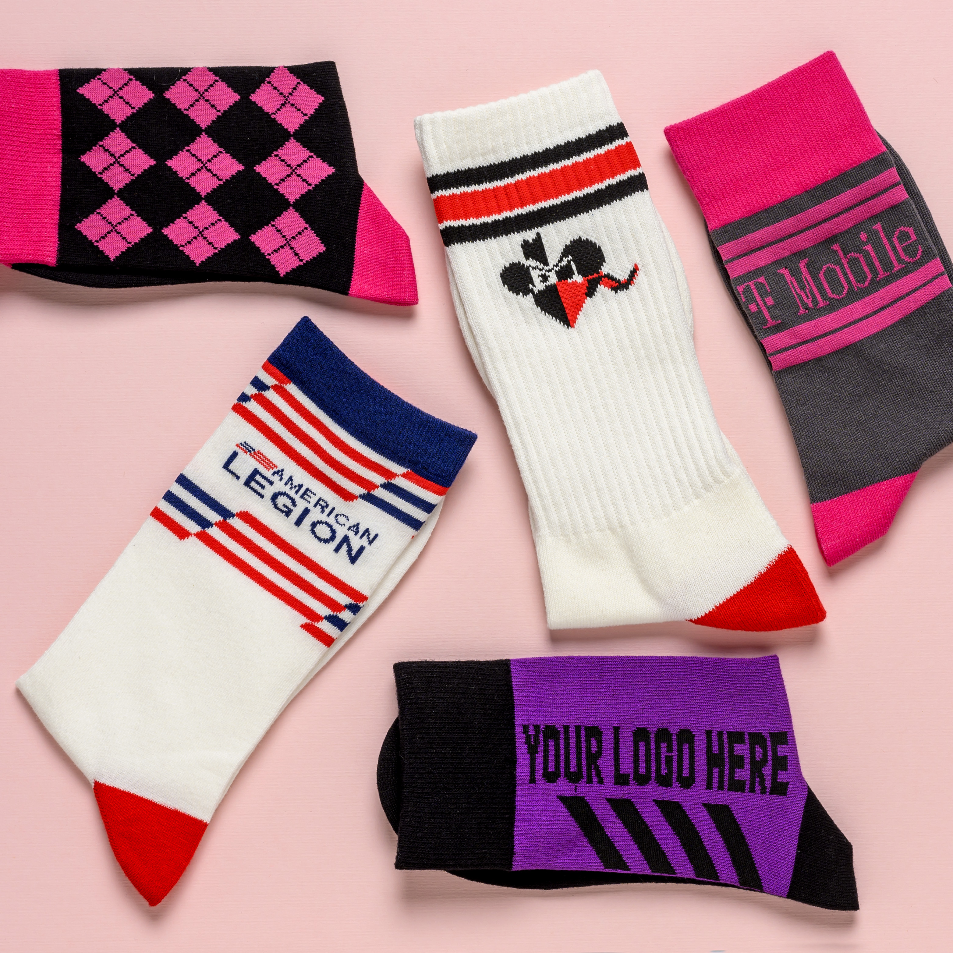 Five different custom-designed socks with various logos and patterns laid flat on a pink surface.