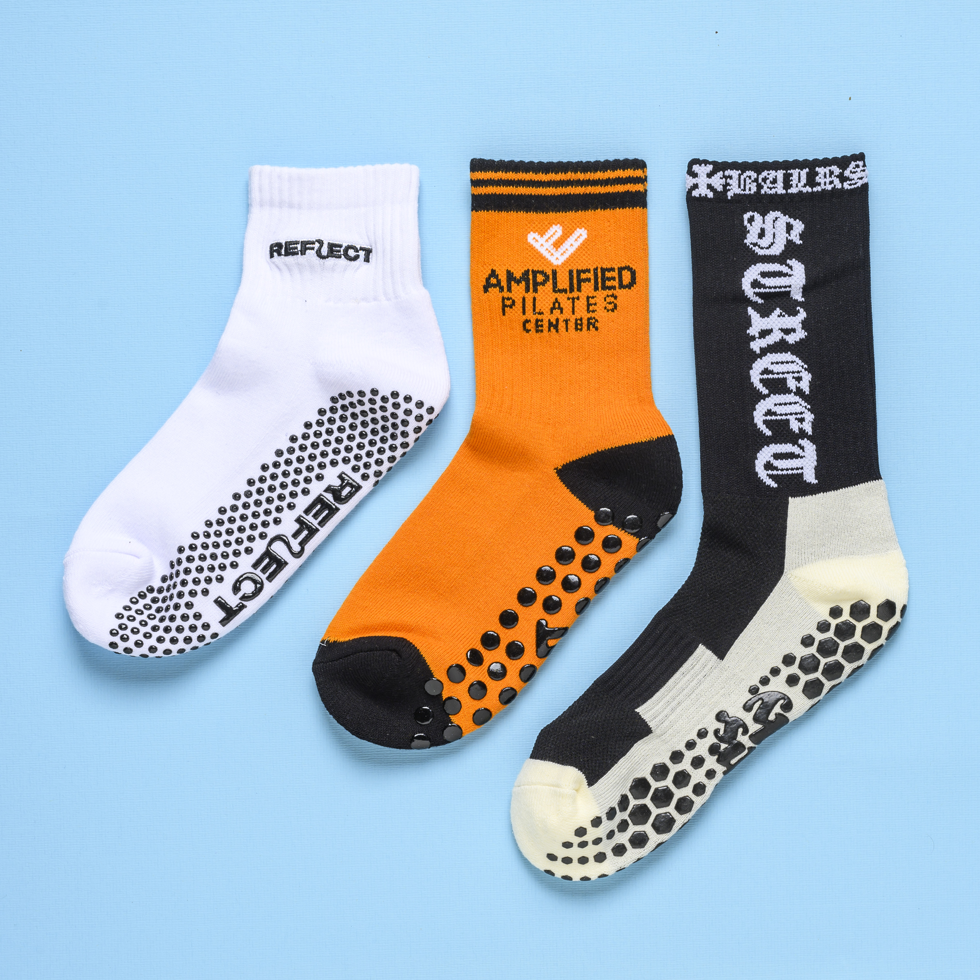 Three different athletic grip socks in white, orange, and black are laid out on a blue background.