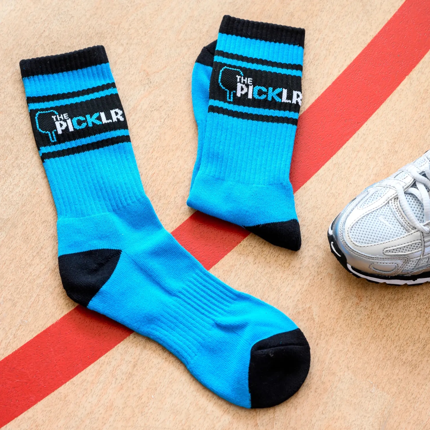 A pair of blue and black athletic socks with 'The Picklr' logo next to a silver sneaker.