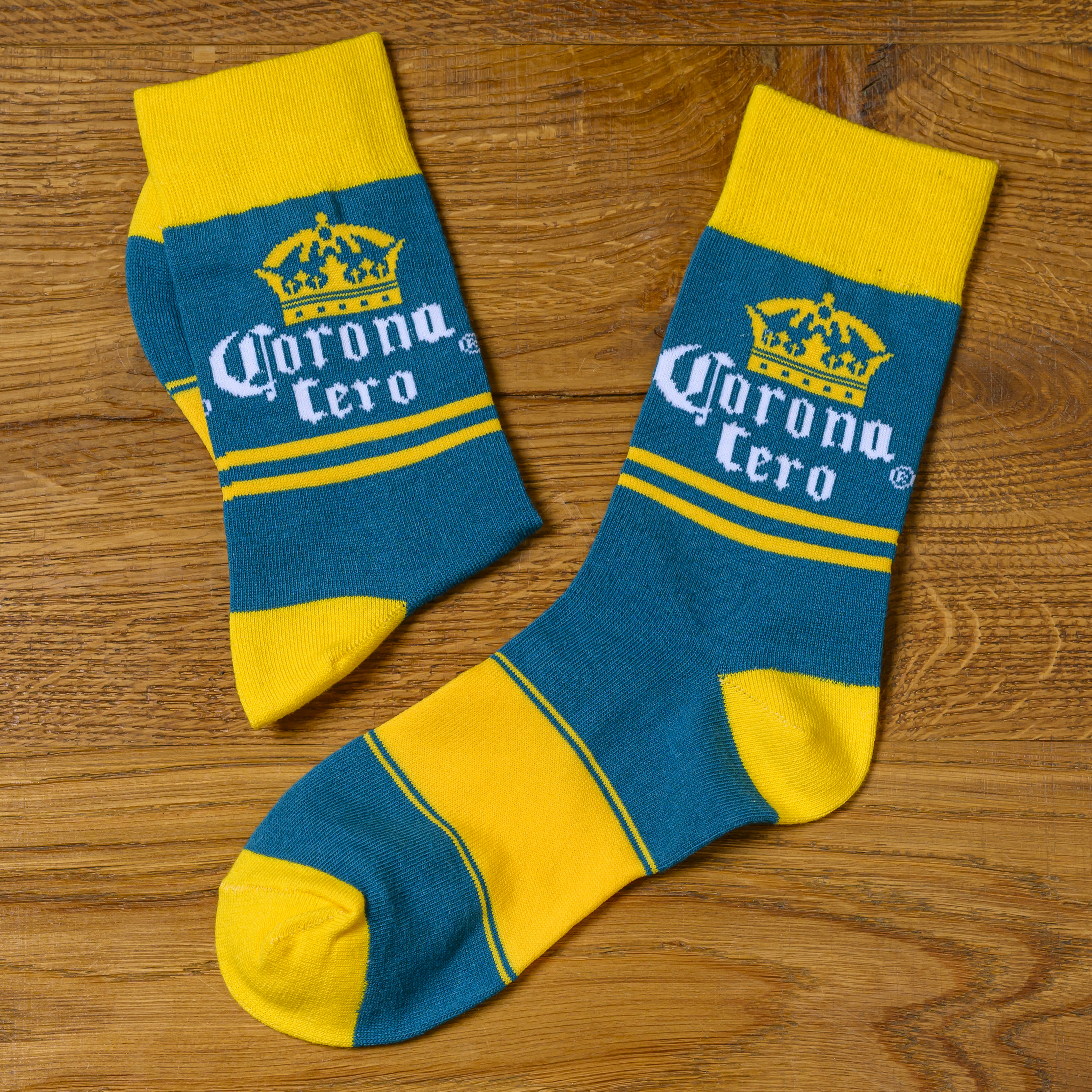 A pair of blue and yellow socks with the Corona Cero logo on a wooden surface.