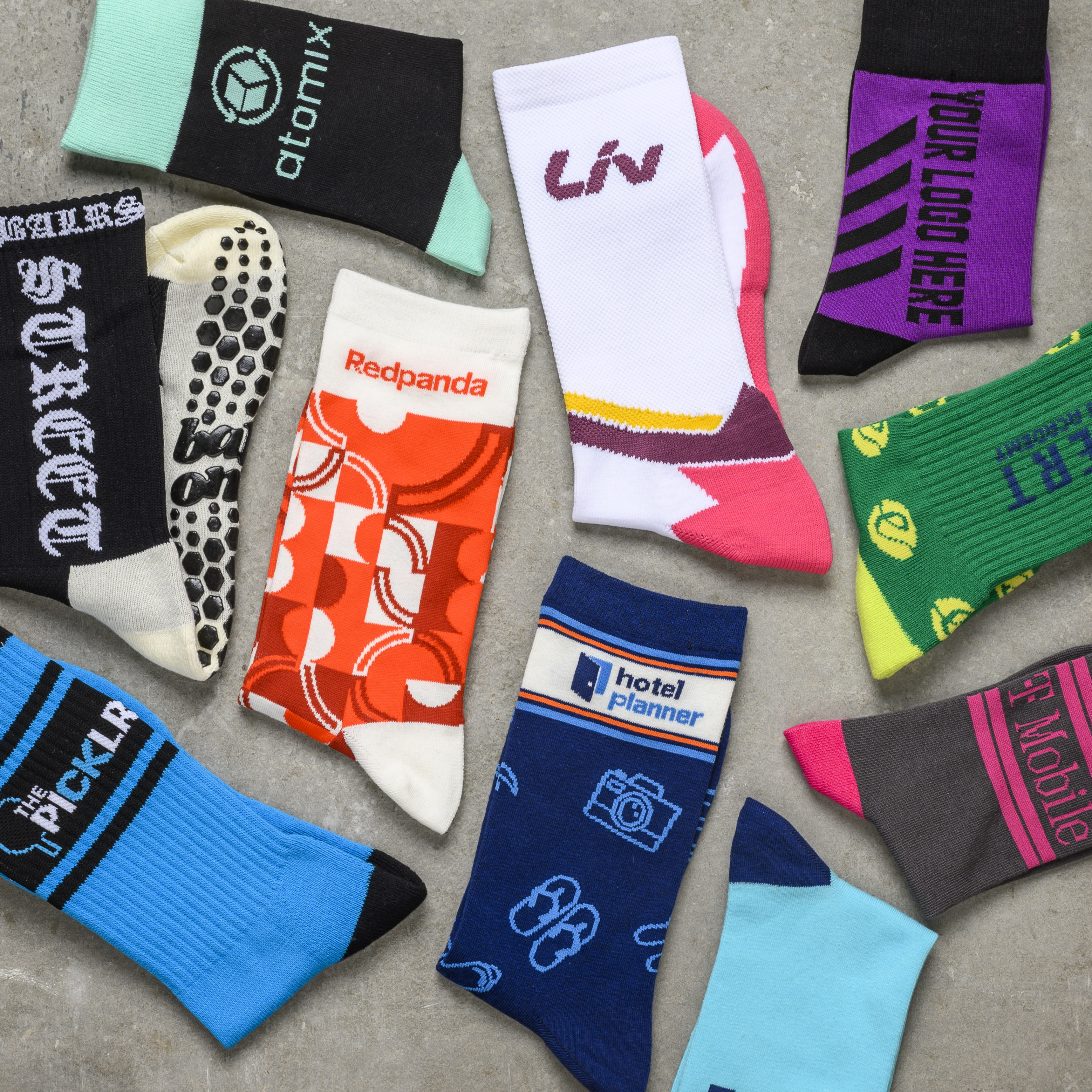 An overhead view of multiple pairs of colorful, custom-branded socks scattered on a gray surface.