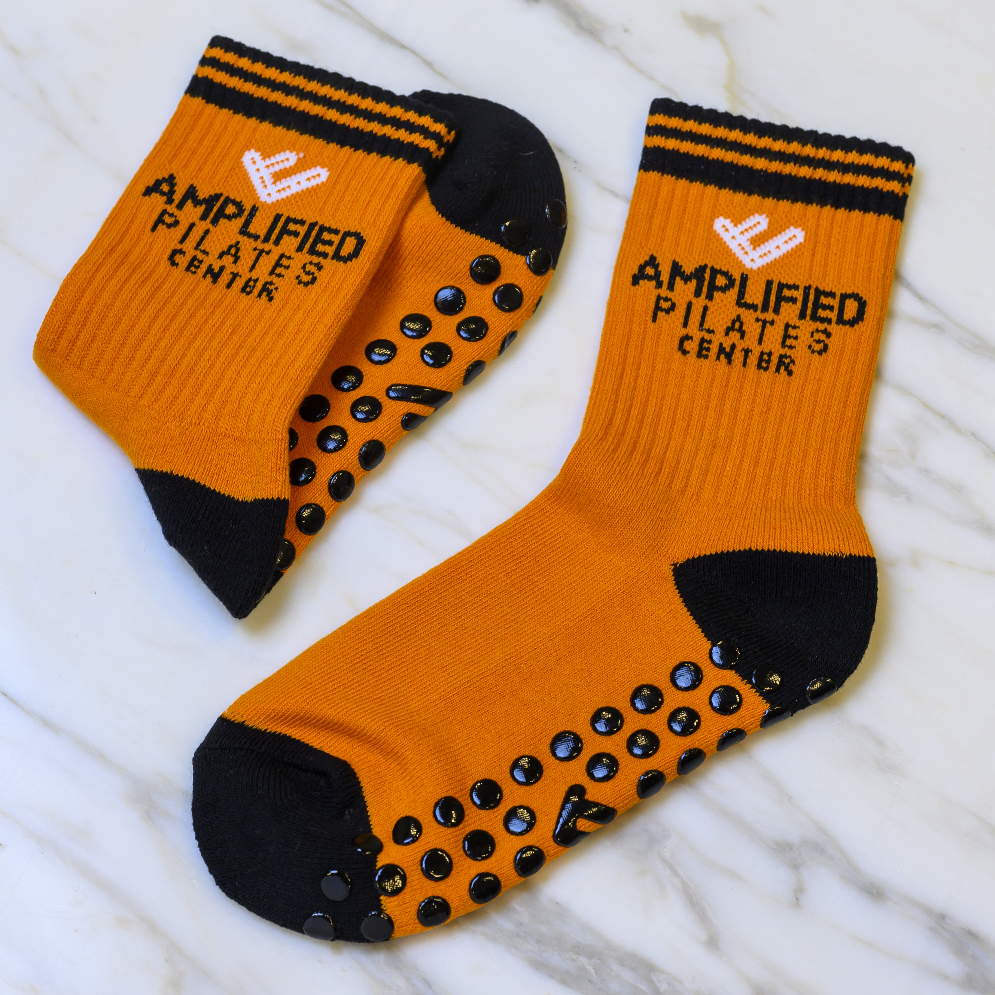 A pair of orange and black grip socks with the words 'Amplified Pilates Center' on them.