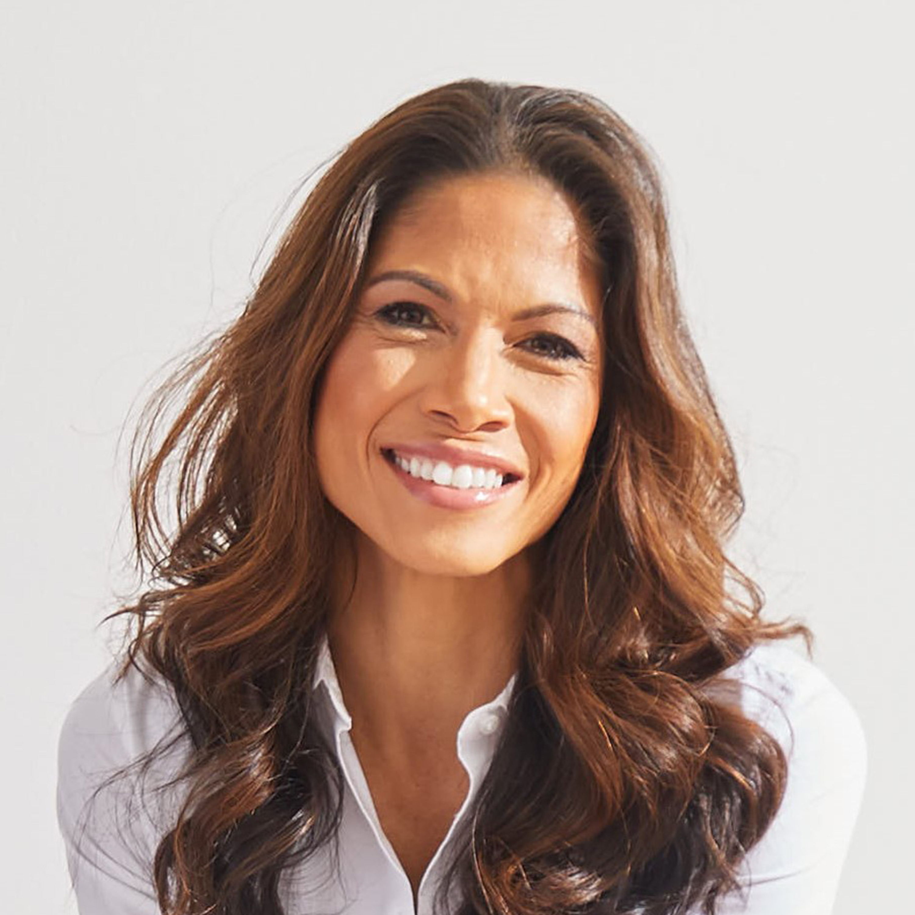 A smiling woman with long brown hair, wearing a white collared shirt, against a white background.