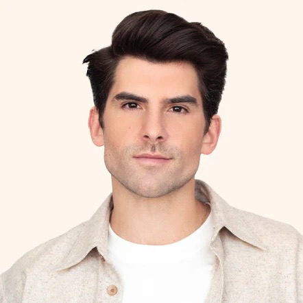 Man with dark hair wearing a beige shirt and white T-shirt, looking at the camera.