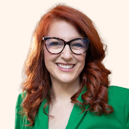 Person with red hair, glasses, wearing a green jacket, smiling at the camera.