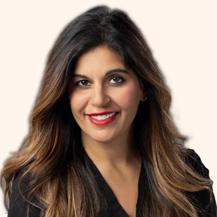 Smiling person with long, wavy dark hair and red lipstick against a plain background.