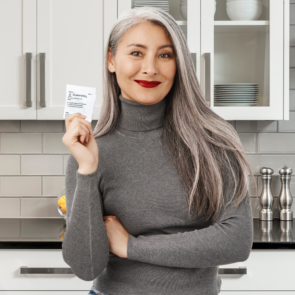 Person with gray hair and turtleneck holding a packet in a kitchen.