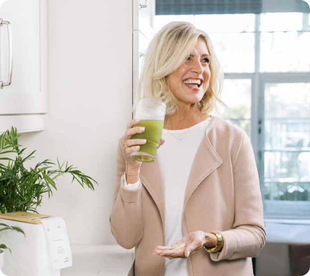 Woman in kitchen holding a glass of green smoothie, smiling.