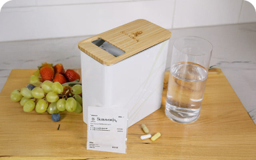 Container with pills, a glass of water, and fruits on a wooden surface.