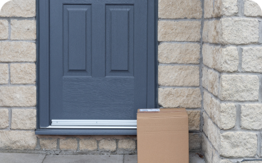 A cardboard package placed in front of a blue door on a stone porch.
