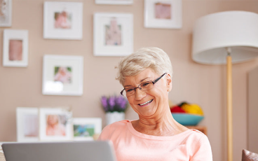 Senior woman smiling while using a laptop at home.