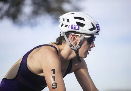 Cyclist wearing a helmet and sunglasses, with number 119 on arm, riding outdoors.