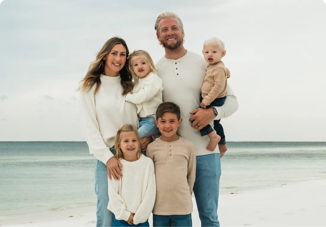 Family of six posing on a beach with ocean in background.