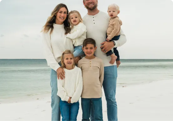 Family of six posing on a beach with ocean in the background.