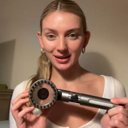 Person holding a shower head, smiling at the camera.