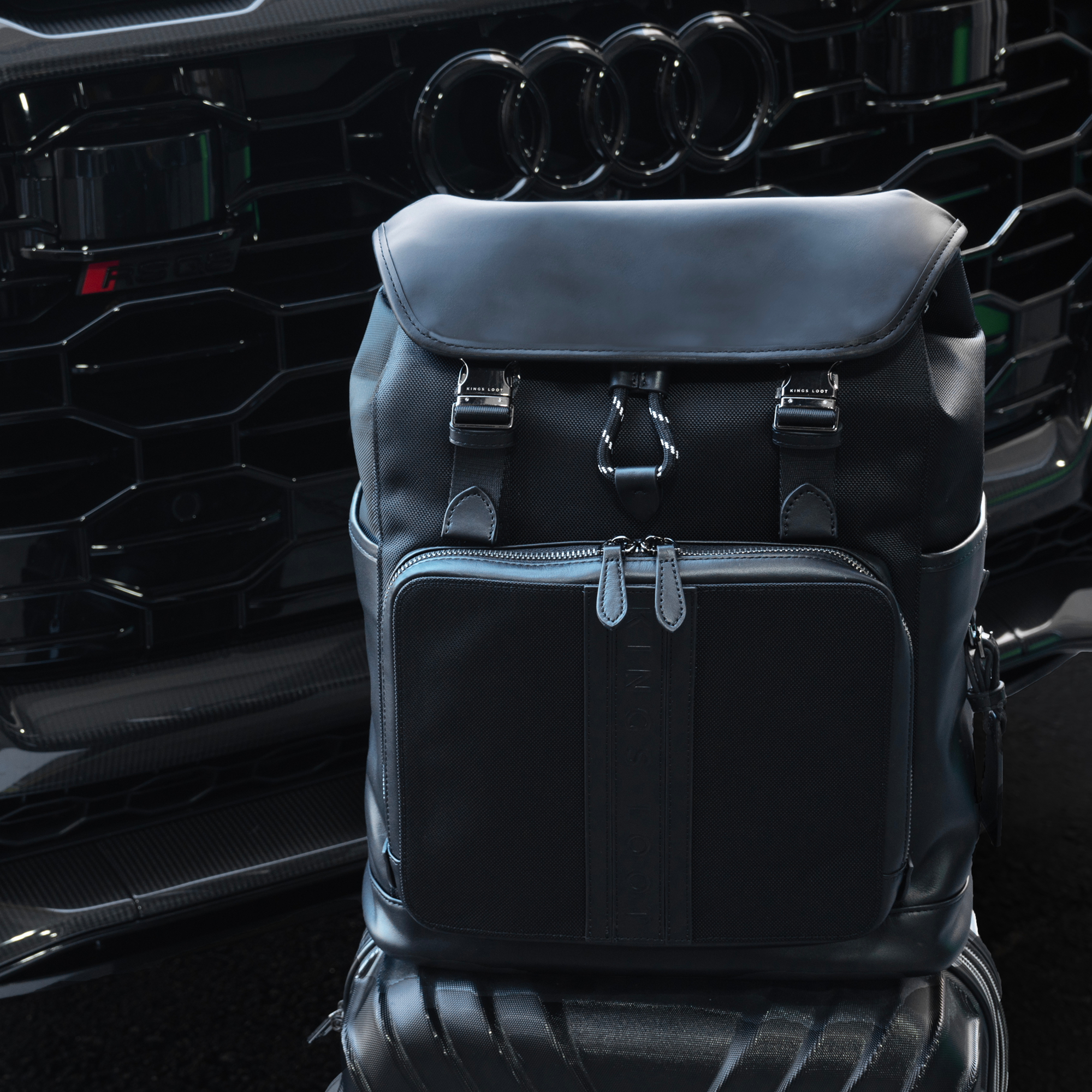 Black backpack in front of a car grille with four rings logo.