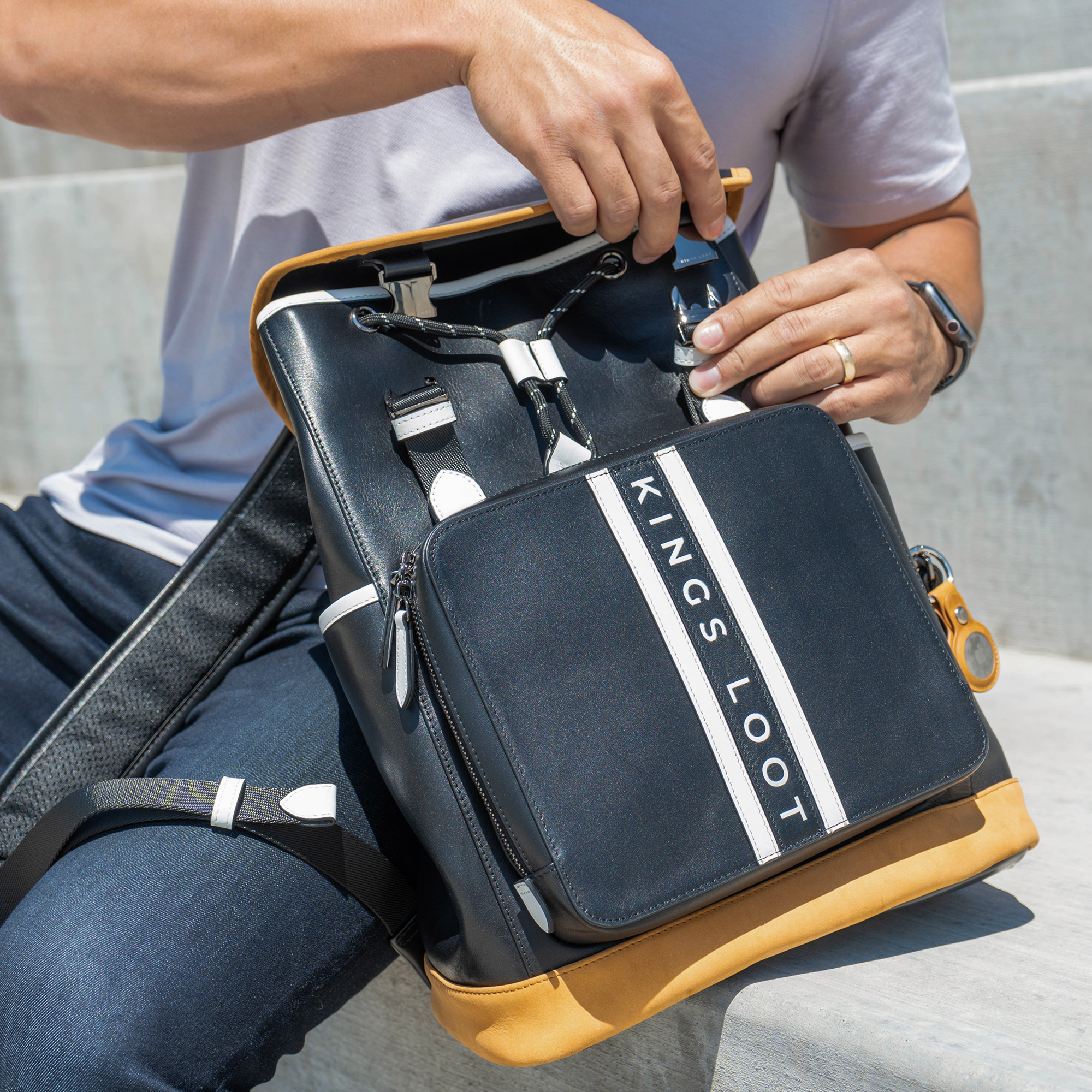 Person opening a black and tan backpack with 'Kings Loot' text.
