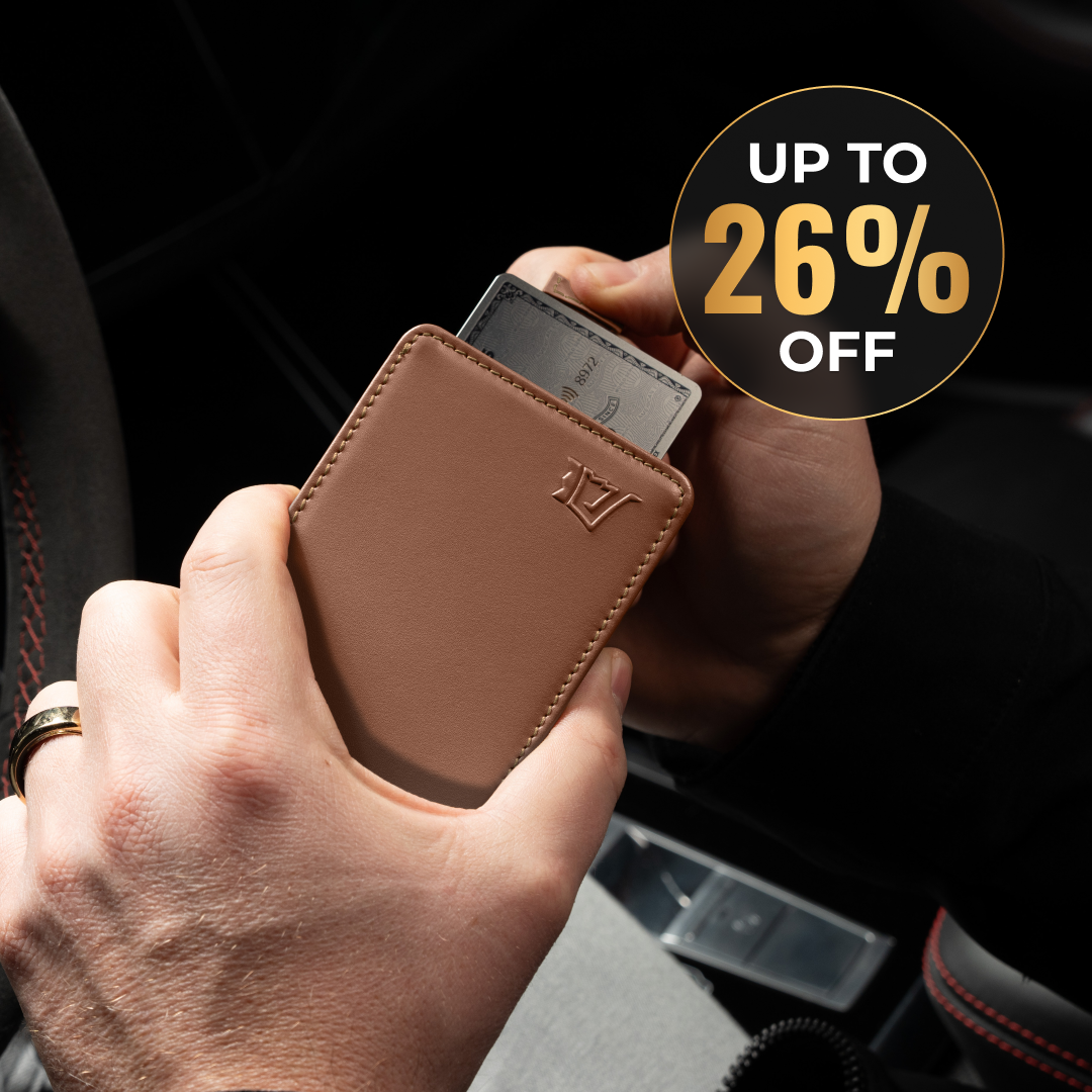 A person's hands hold a brown leather wallet, sliding a credit card into it inside a car.