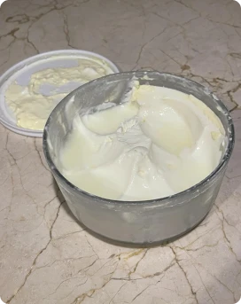 A bowl of thick white cream with a lid on a marble surface.