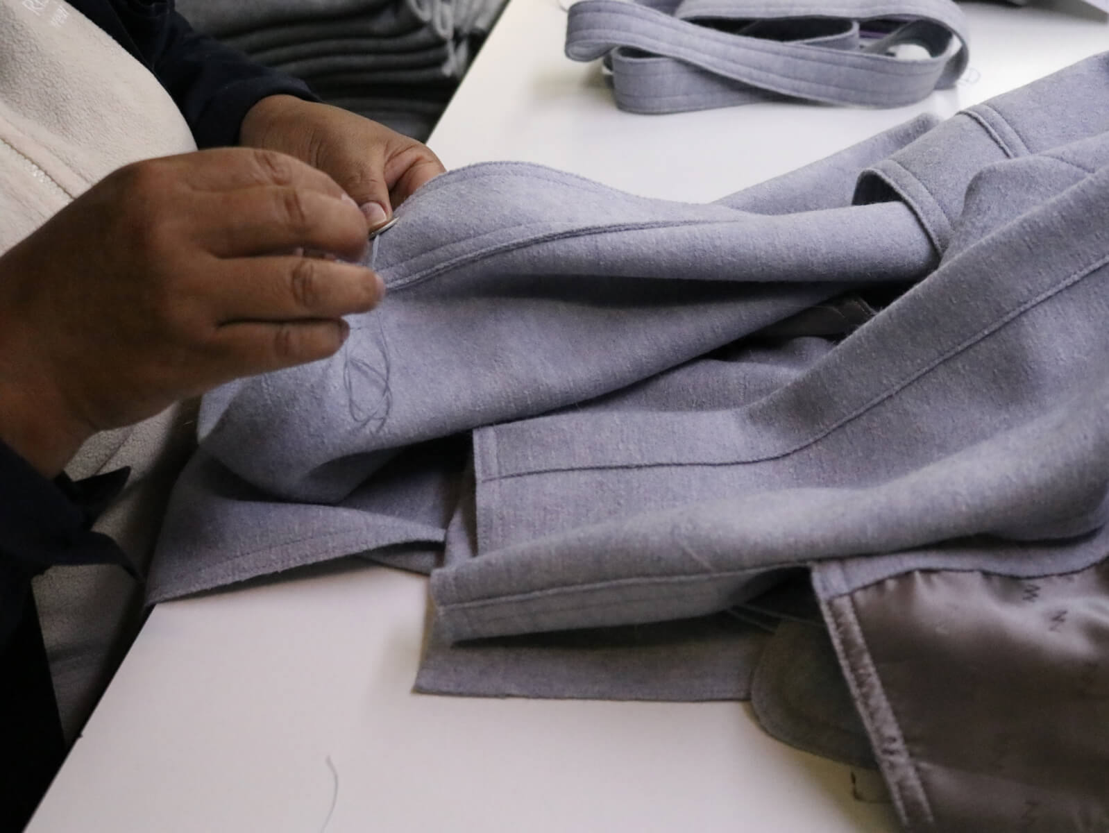 Person hand-sewing a gray fabric garment on a table.