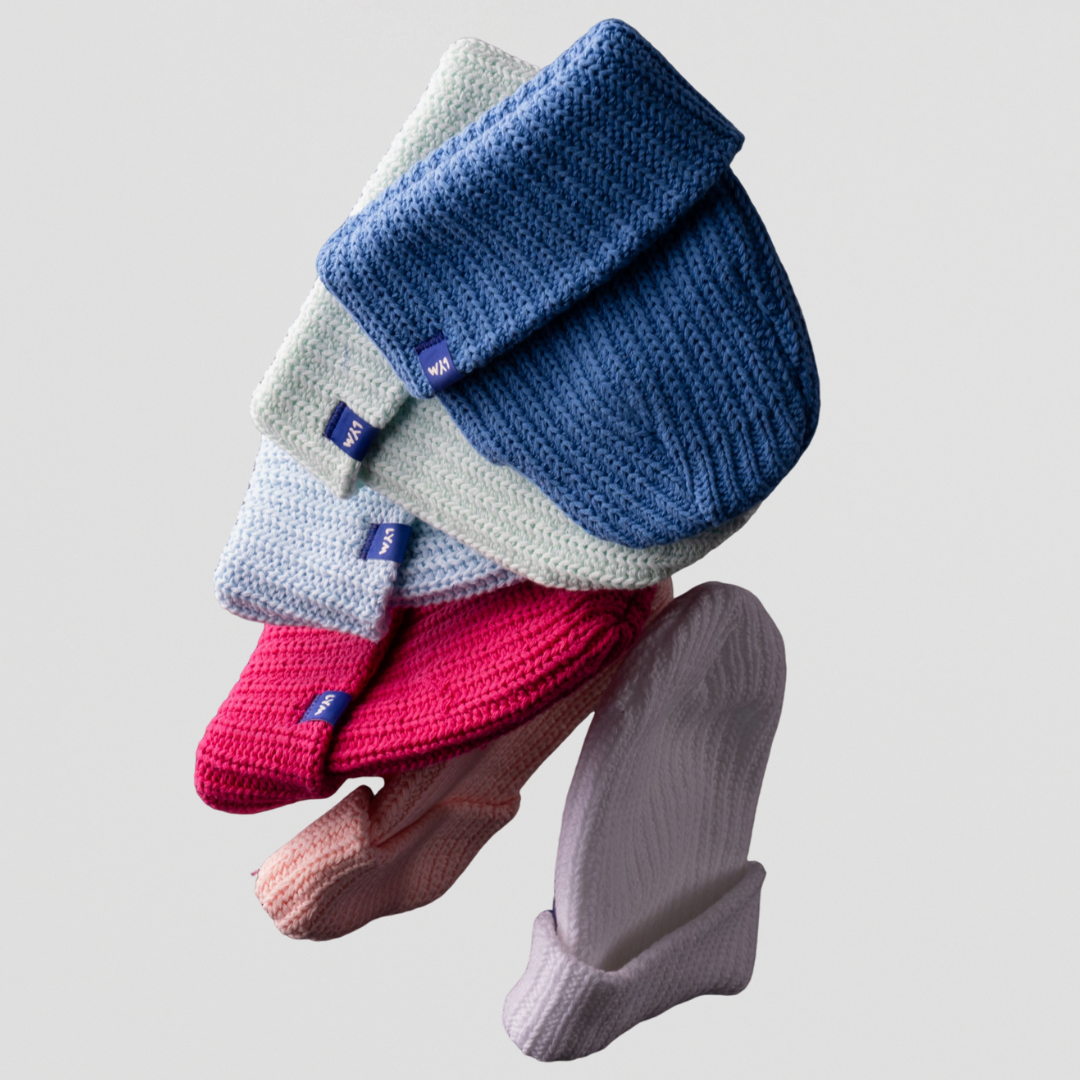 A stack of six colorful, cuffed knit beanies floating against a light grey background.