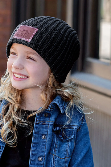 A smiling young girl with long blonde hair wears a black ribbed beanie and a denim jacket.