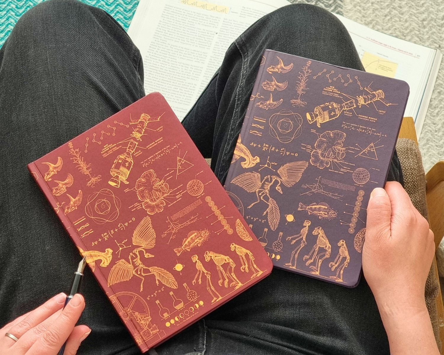 Two notebooks with scientific illustrations held by a person sitting with a book.