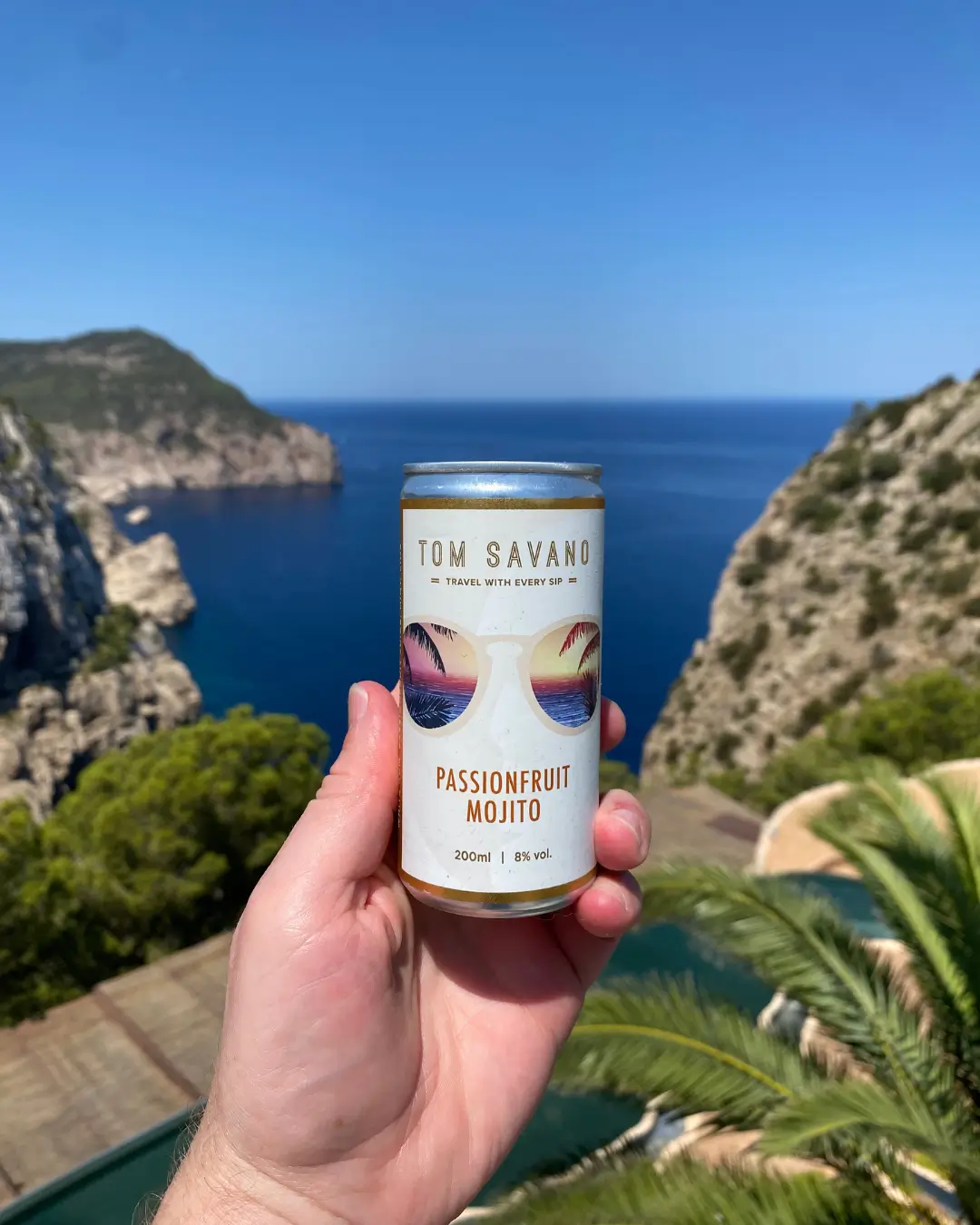 Hand holding a can of passionfruit mojito with a scenic ocean view.