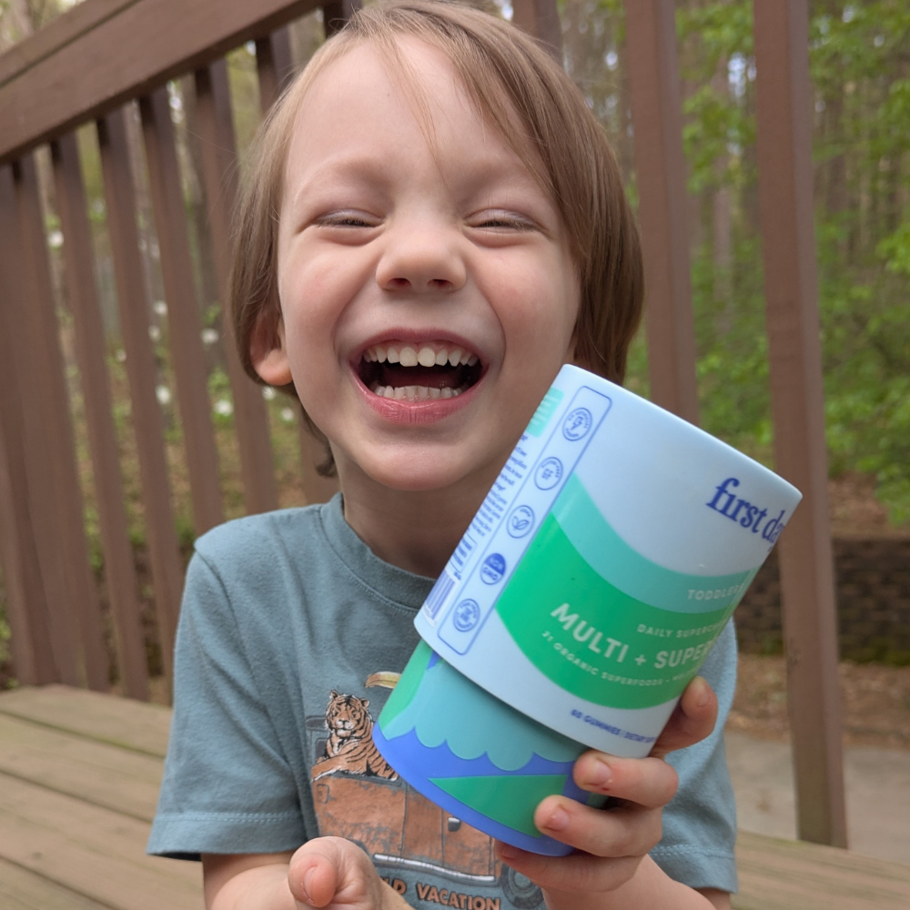 Child laughing and holding a container on a wooden deck.
