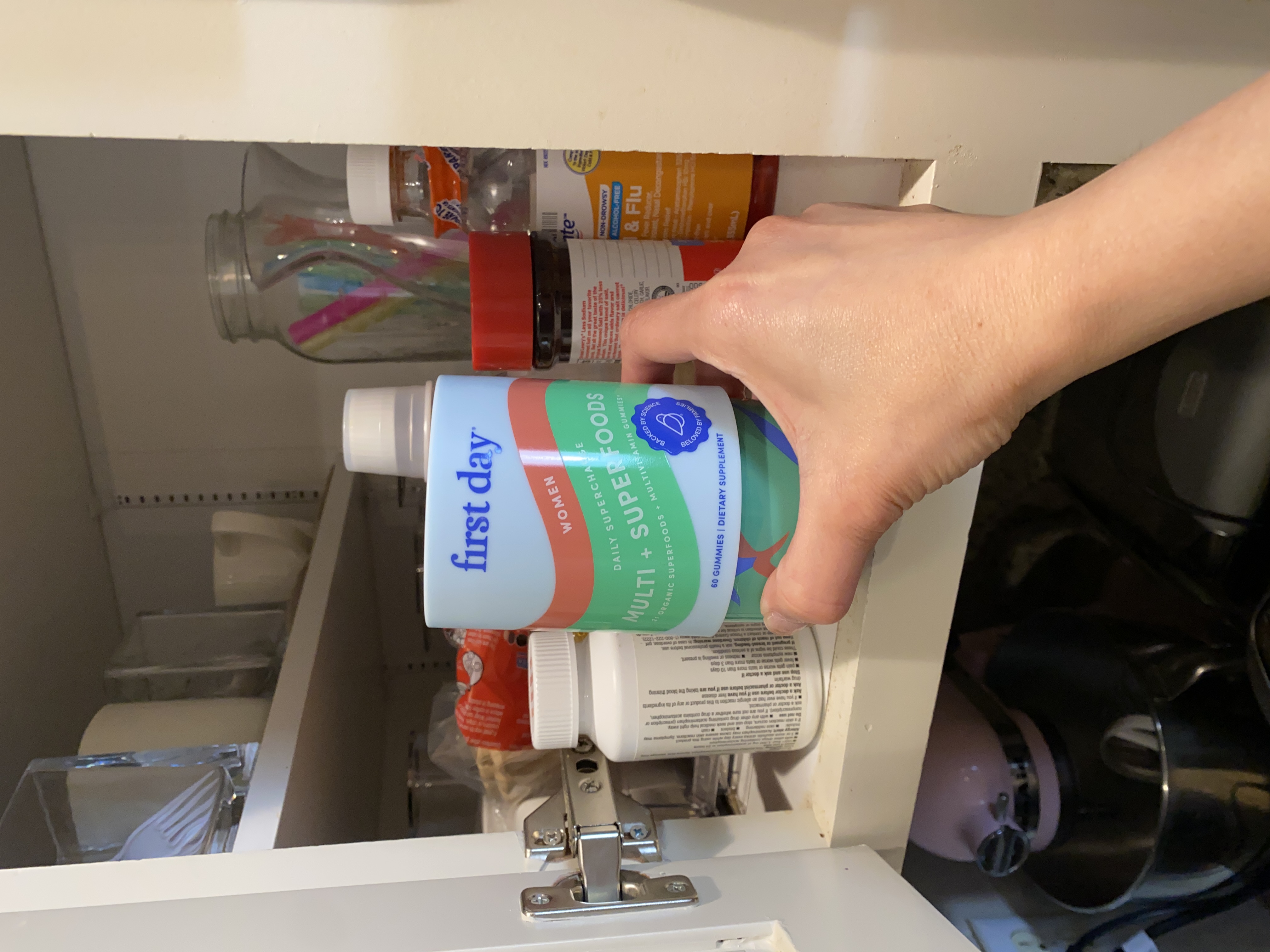 Hand holding a container of dietary supplements in a kitchen cabinet.