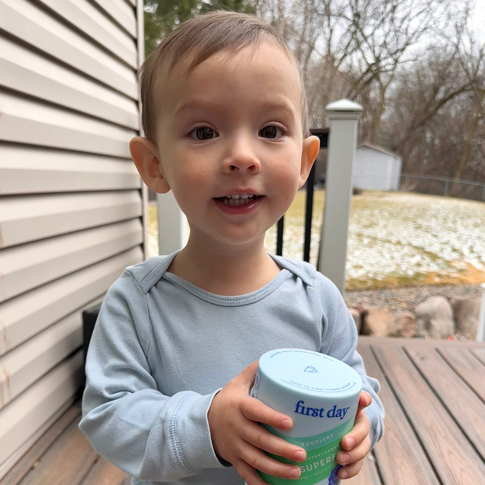 Young child holding a container on a porch with a snowy yard in the background.
