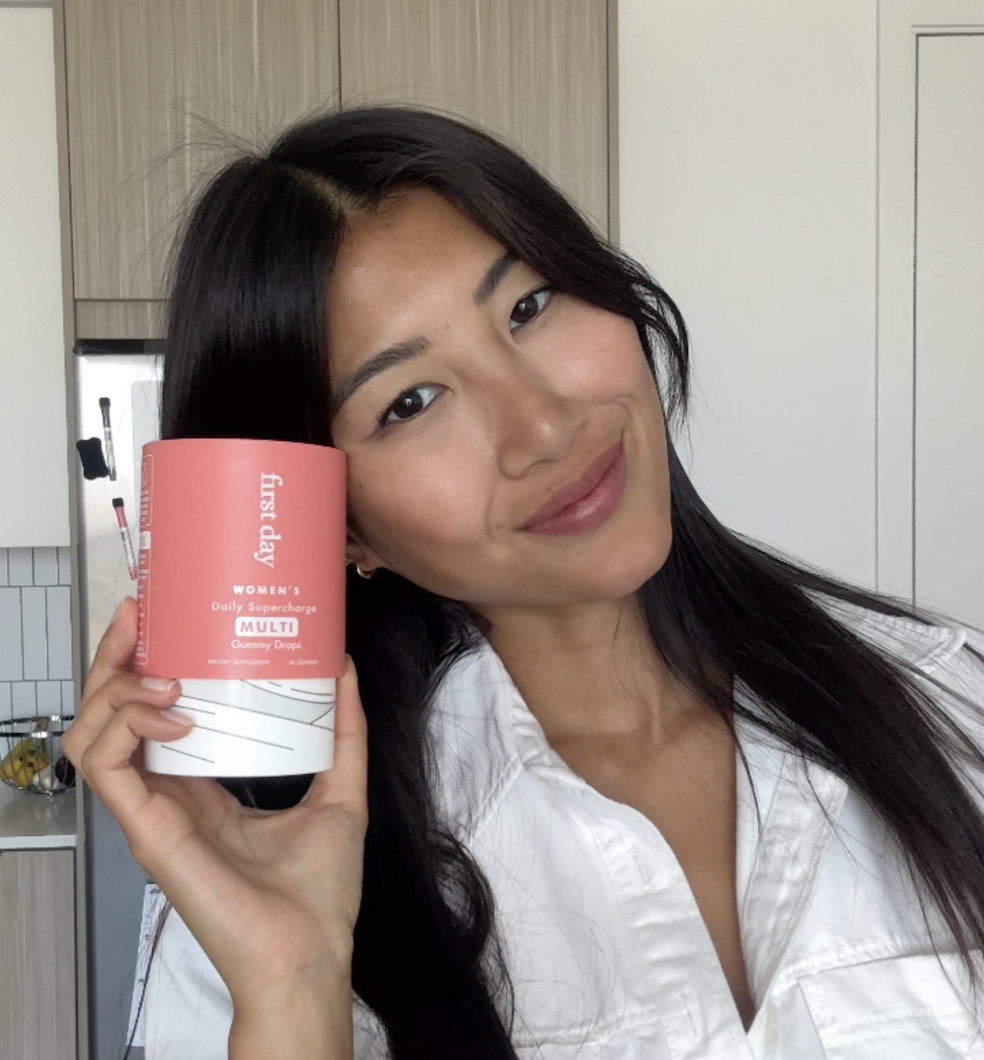 Person holding a container labeled 'Women's Daily Supercharge Multi Gummy Drops' in a kitchen.