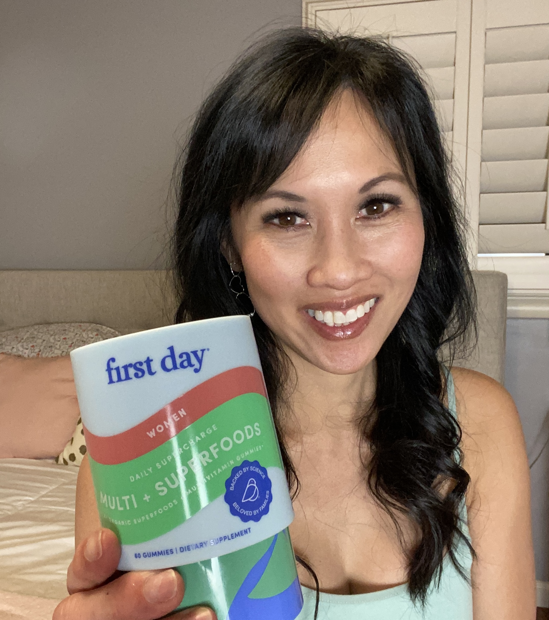 Person smiling and holding a container labeled 'first day' dietary supplement.
