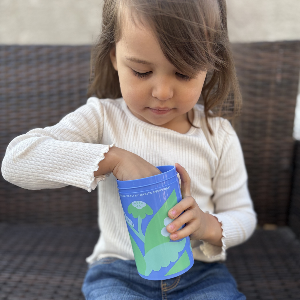 Child in white shirt reaching into a blue cup with green design.