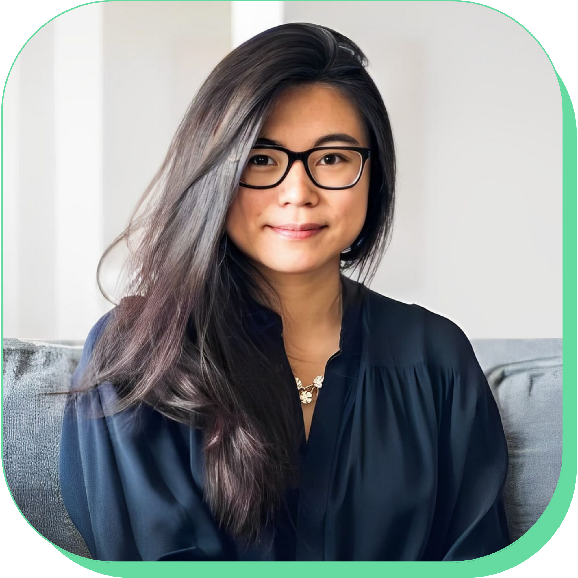 Person with long hair and glasses, wearing a dark shirt, sitting on a couch.