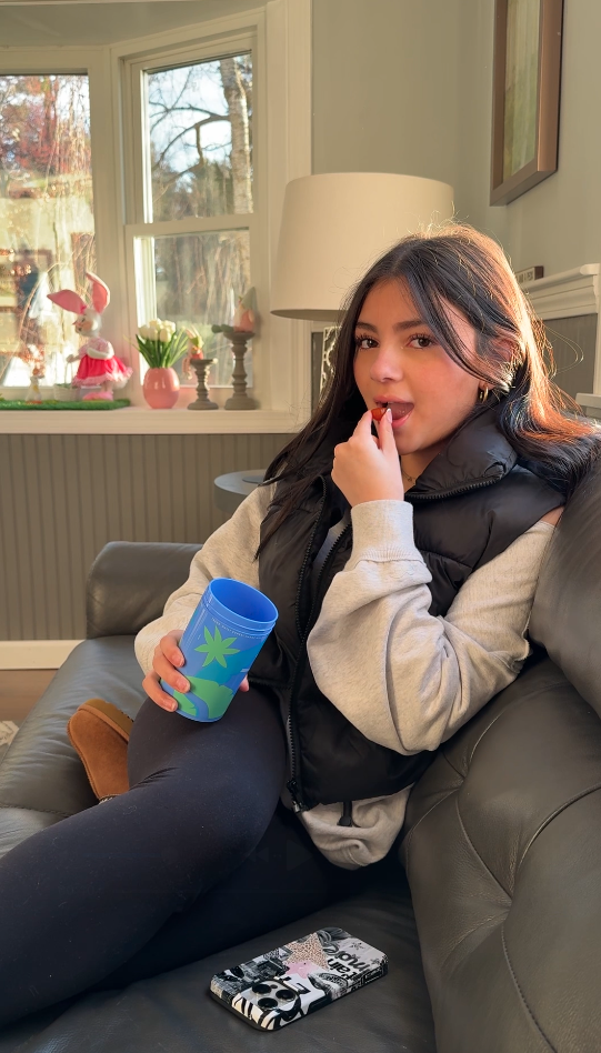 Person sitting on a couch holding a blue cup, with a phone nearby.