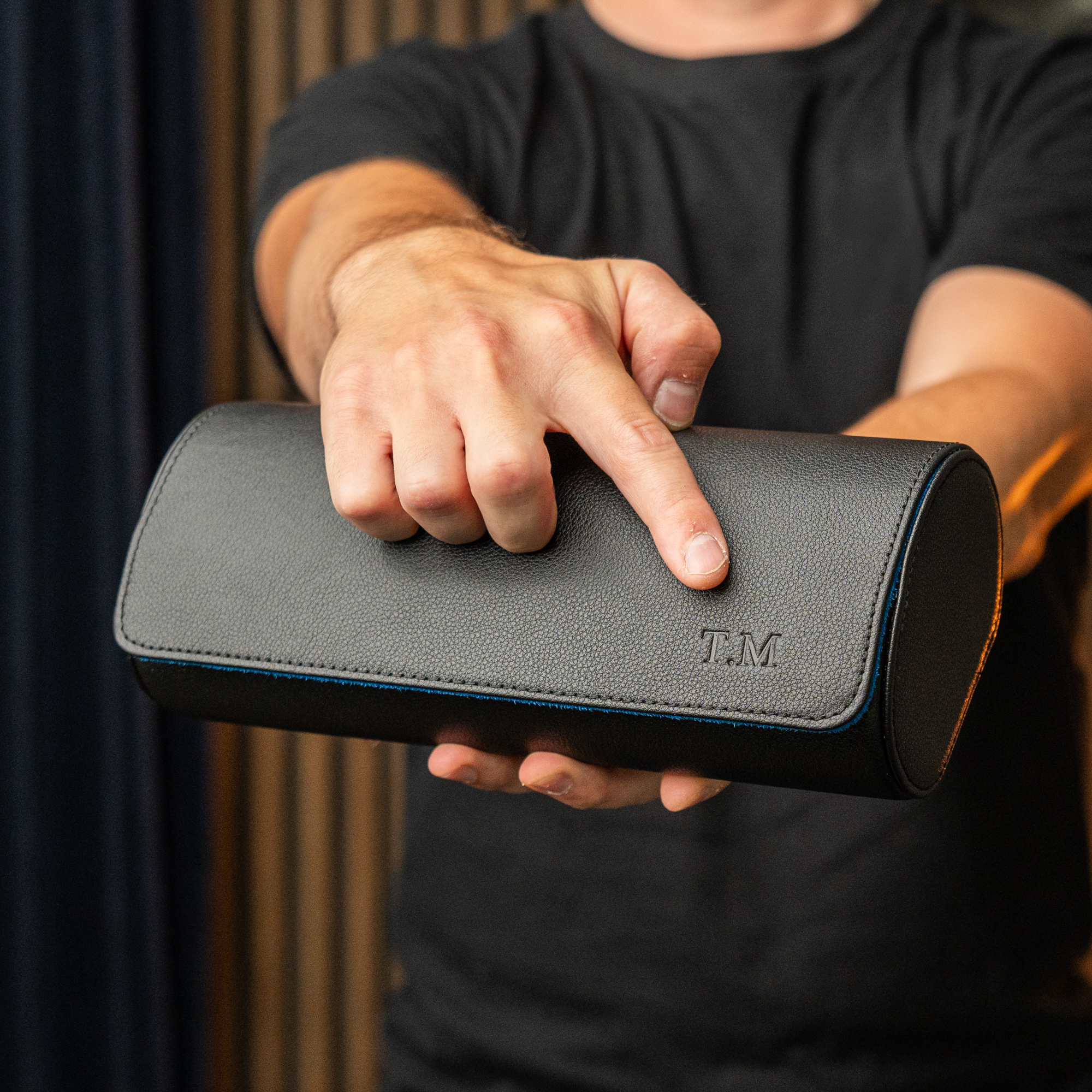 A man points to the initials T.M. embossed on a black pebbled leather case he is holding.