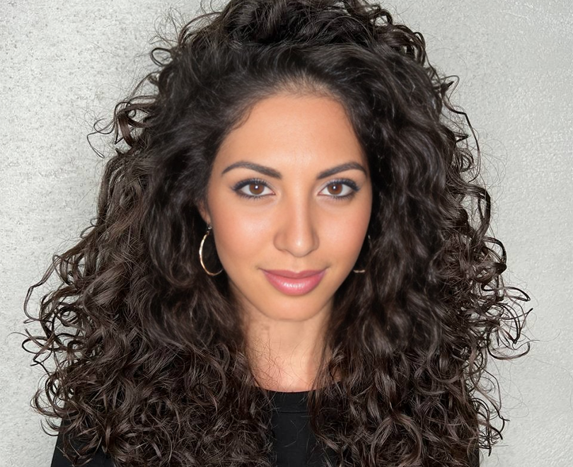 Woman with curly hair and hoop earrings against a gray background.