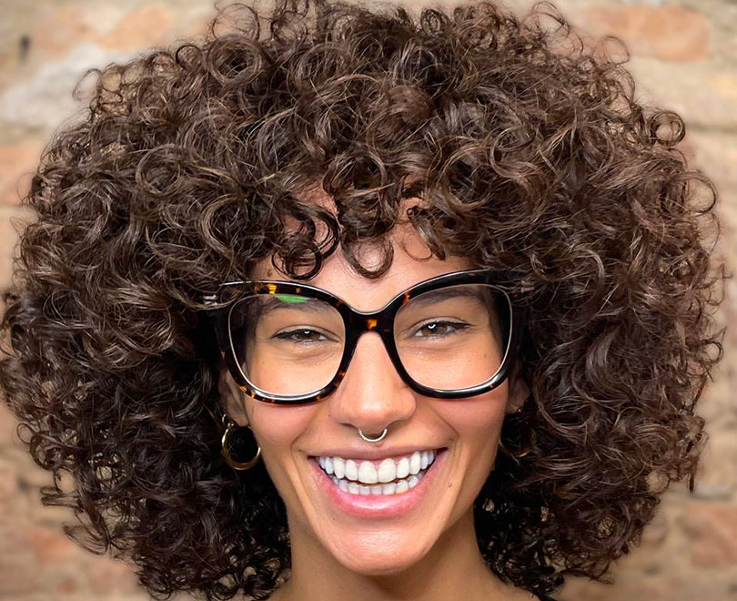 Person with curly hair, large glasses, and a nose ring smiling.