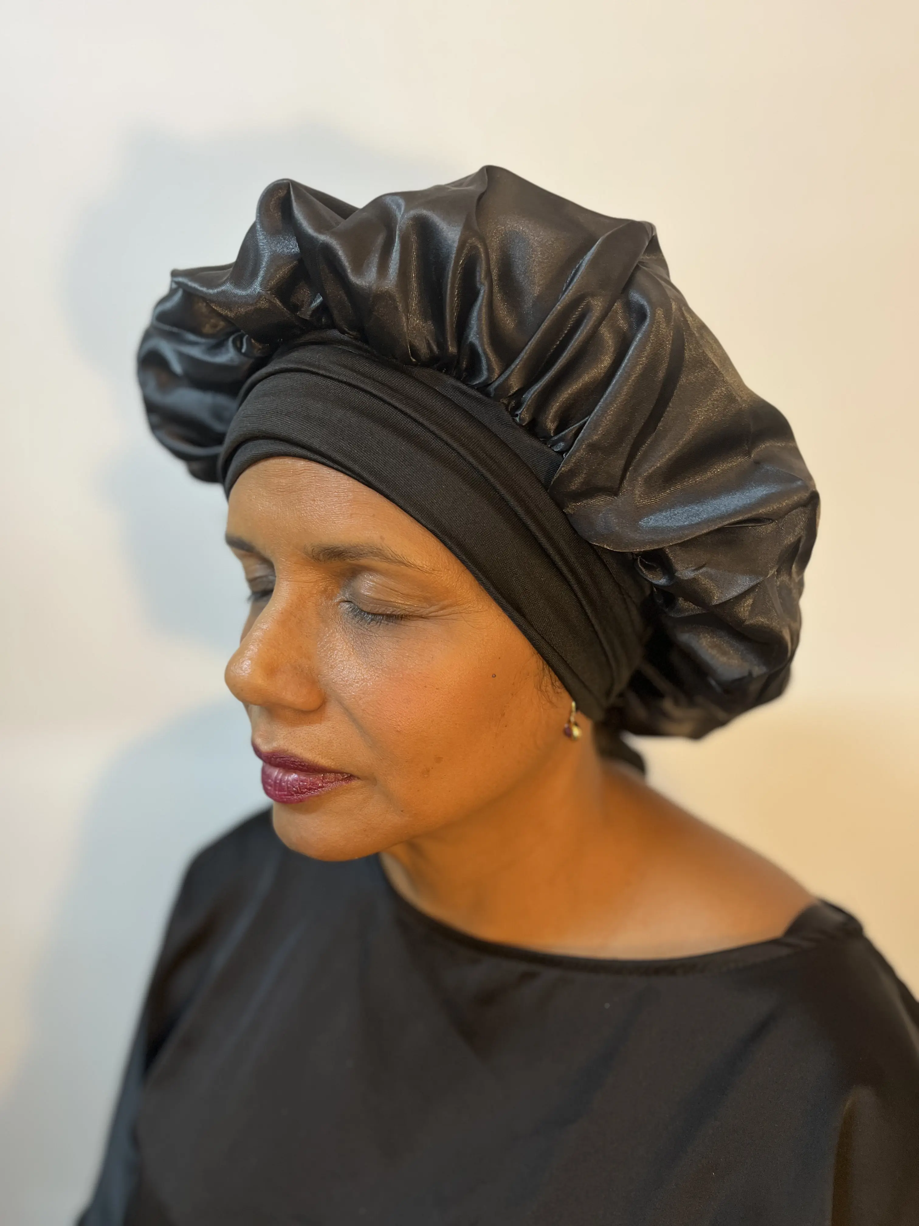 Person wearing a black satin bonnet and matching robe, eyes closed.