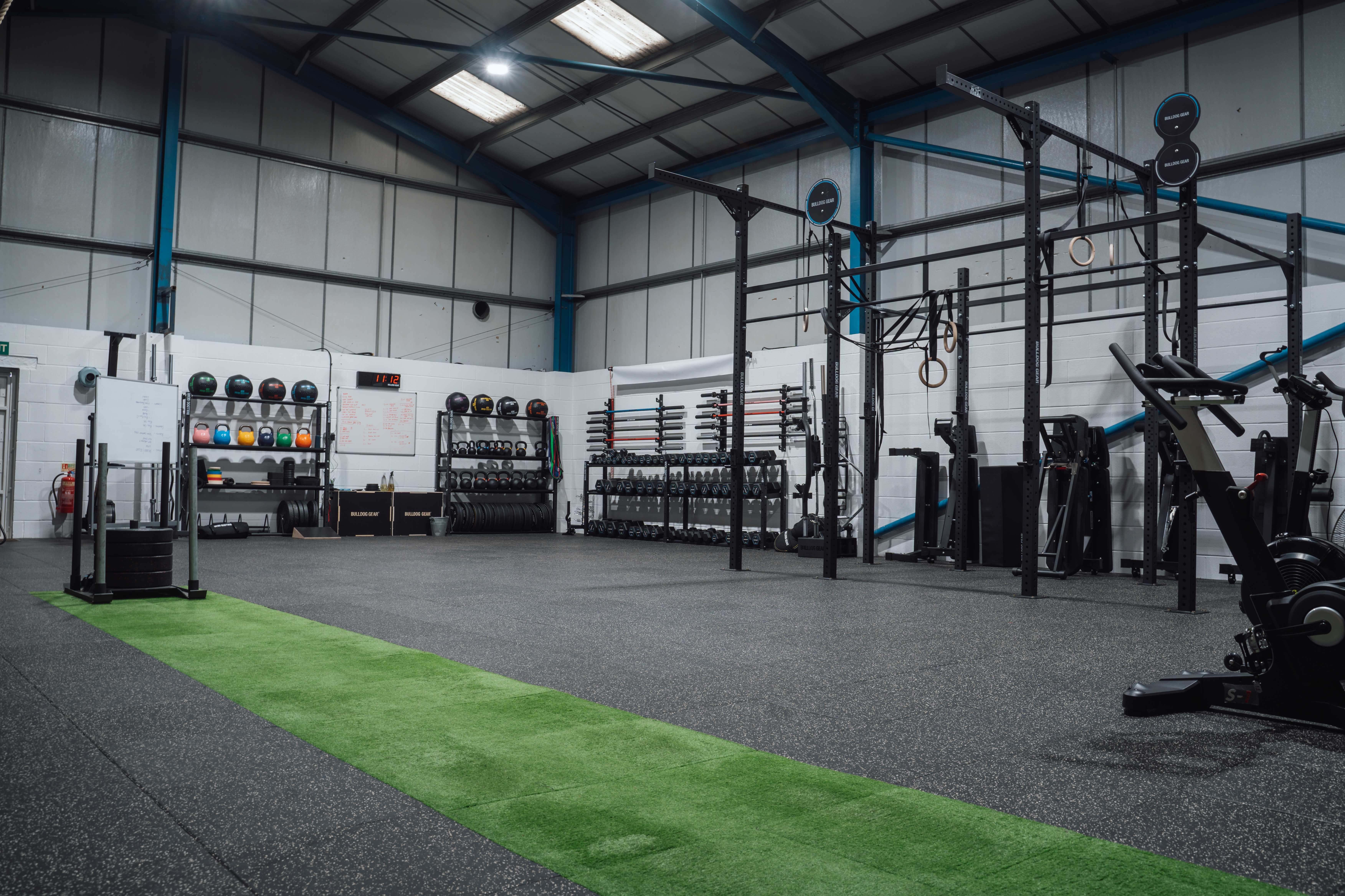 Spacious gym with equipment, weights, and a green turf strip.