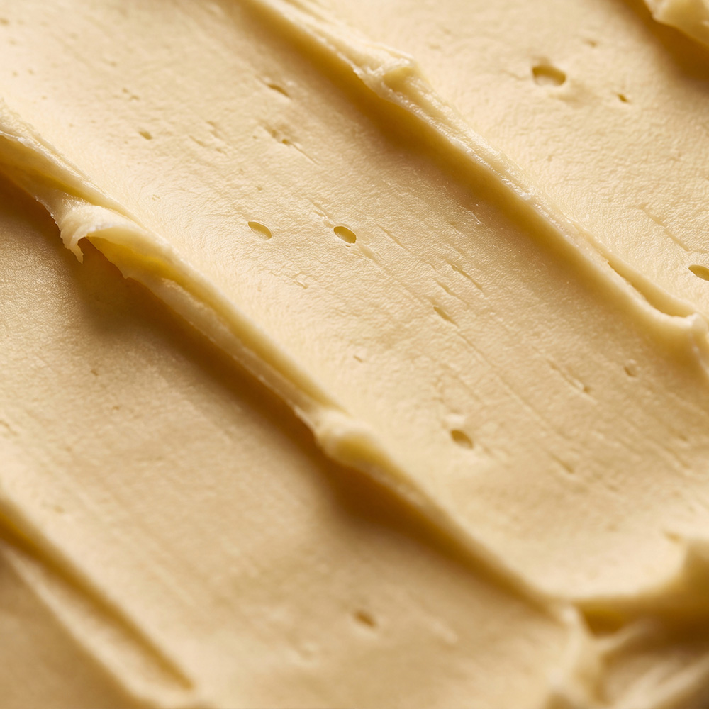 A close-up, macro view of a creamy, pale yellow spread with diagonal texture.
