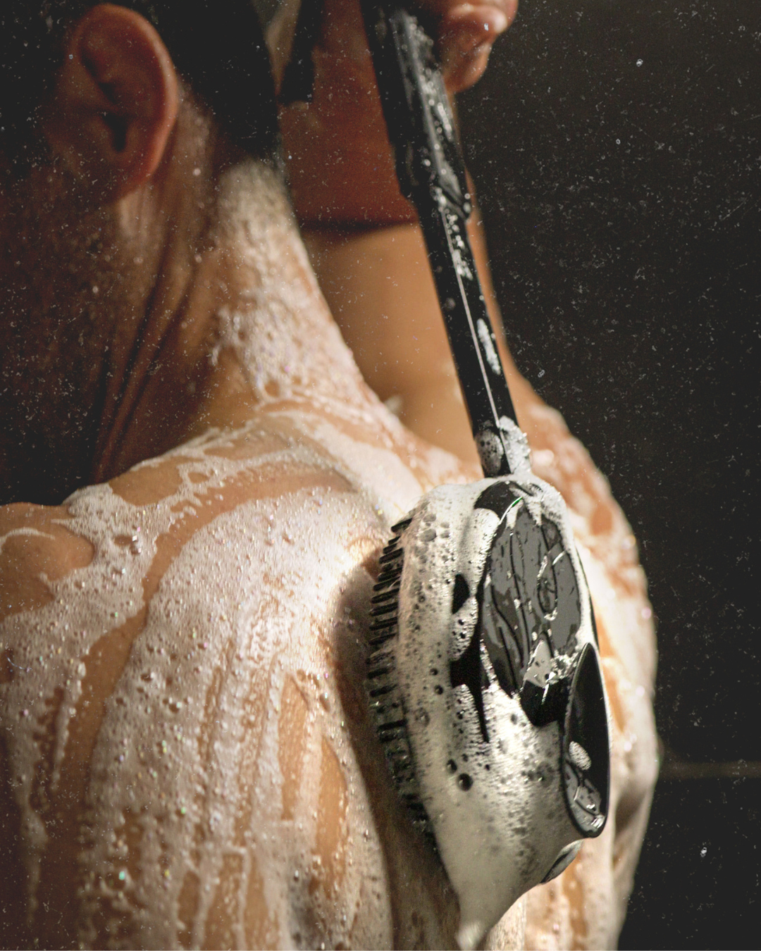 Person washing their back with a soapy brush in the shower.